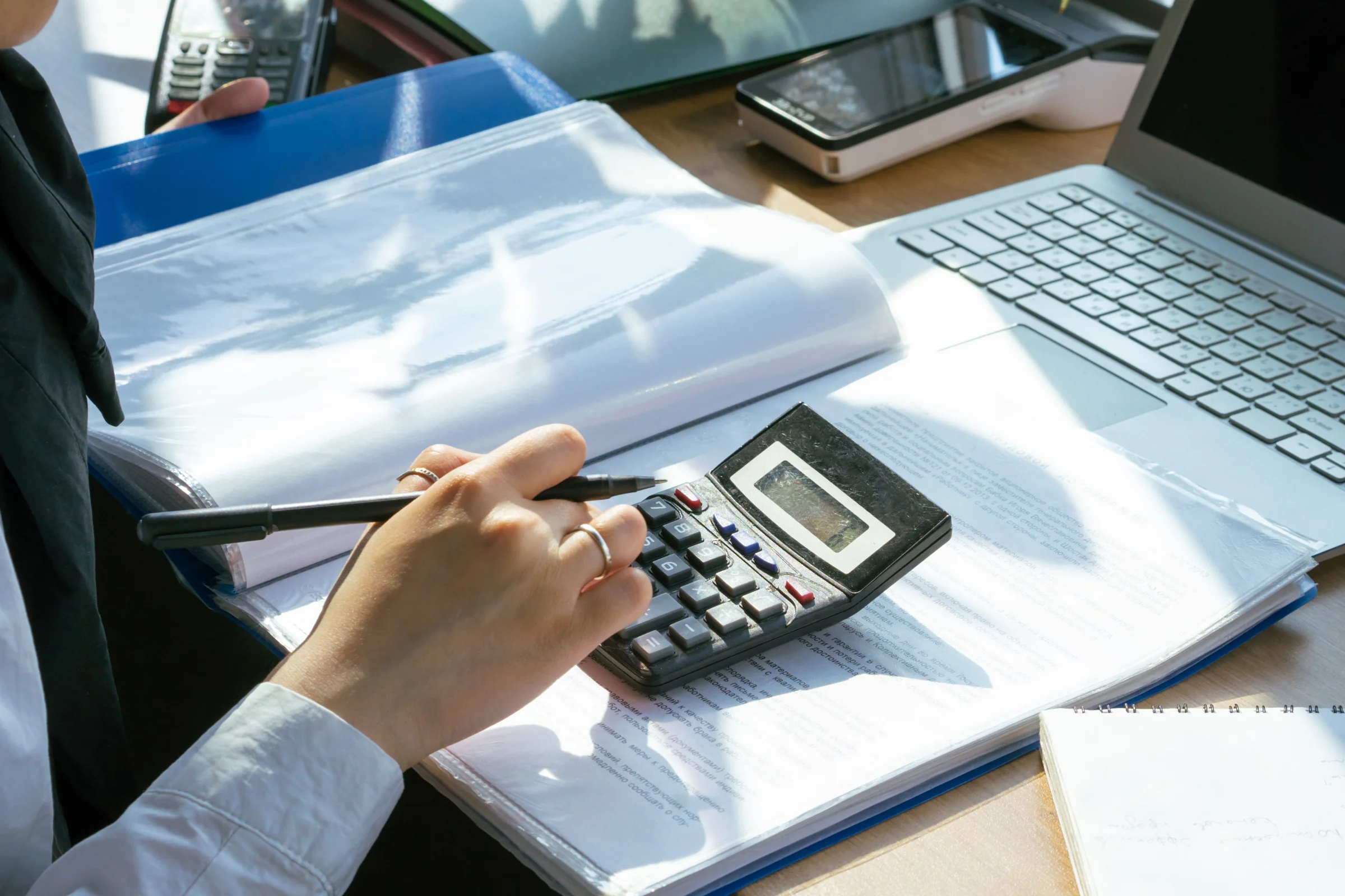 Pessoa trabalhando com calculadora, documentos financeiros e laptop em uma mesa.