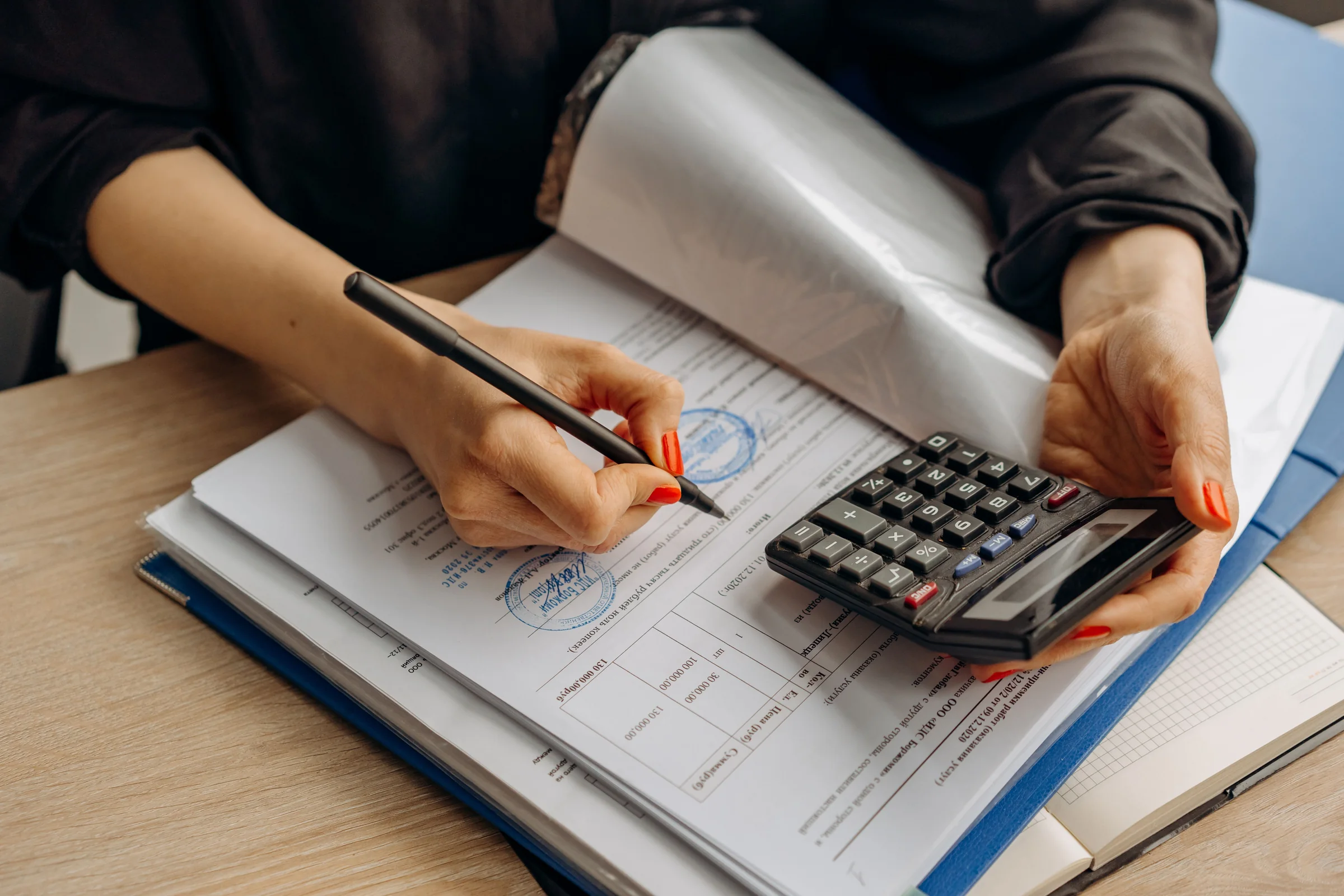 Profissional revisando documentos com uma calculadora sobre a mesa.