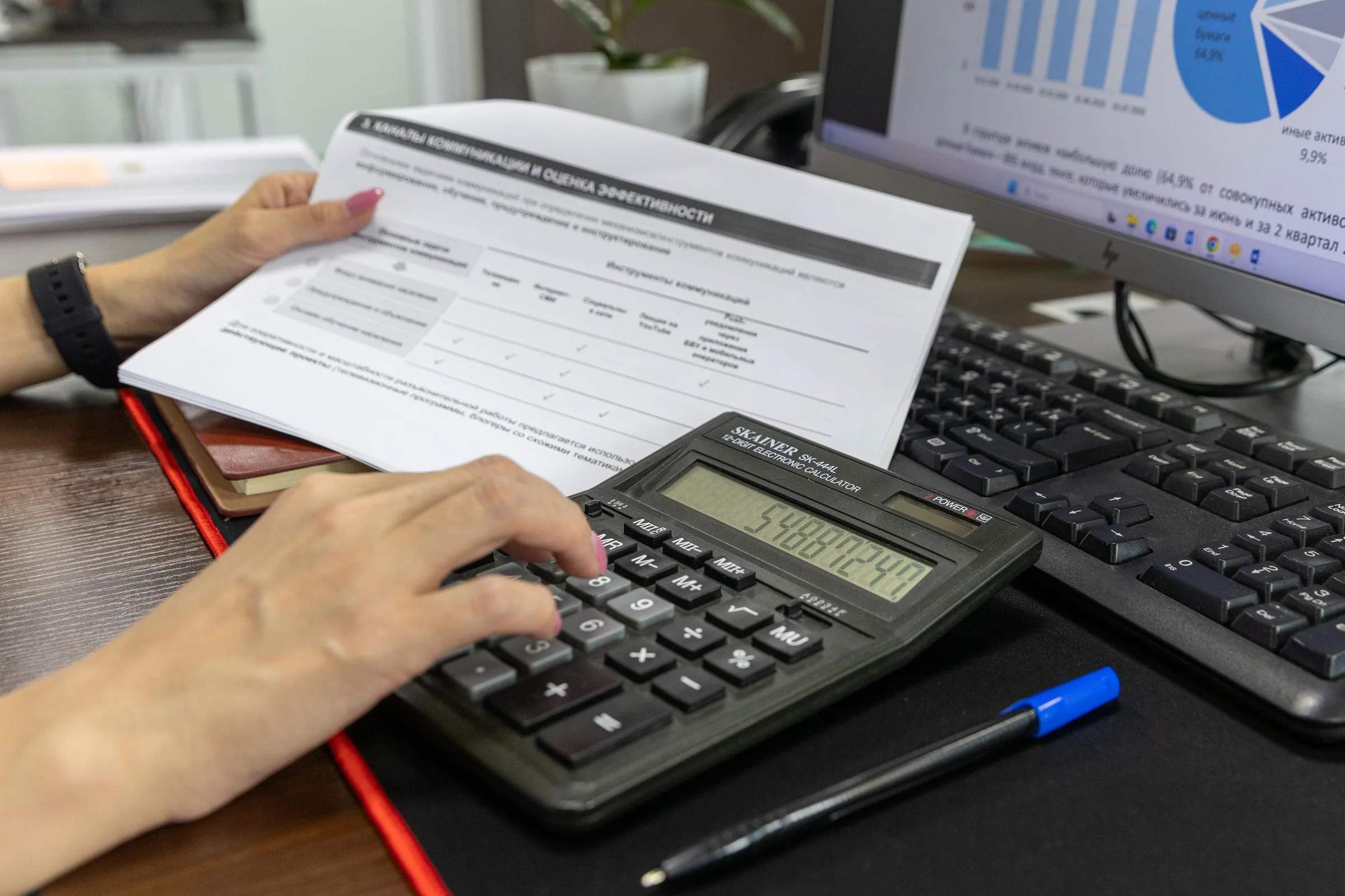 Profissional calculando dados financeiros em documentos sobre uma mesa de escritório.